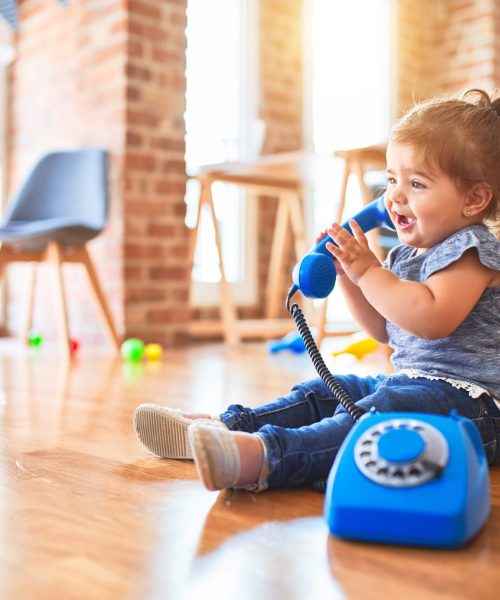Beautiful toddler sitting on the floor playing with vintage phone at kindergarten Beautiful toddler sitting on the floor playing with vintage phone at kindergarten